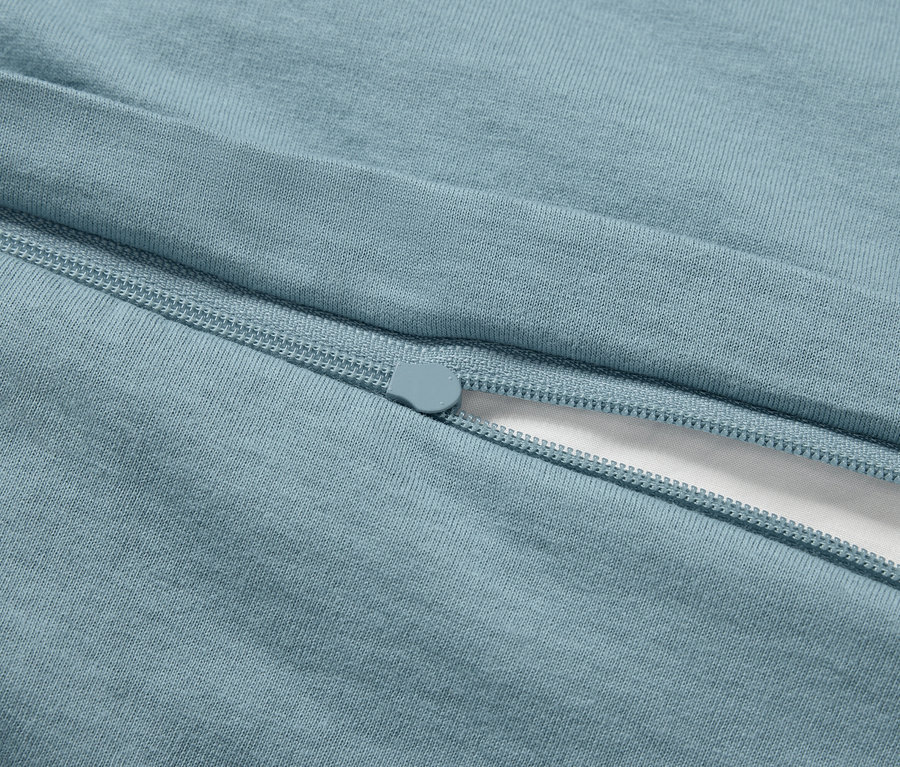 Detail světle modrého povlečení se zipem a kouskem bílé látky.