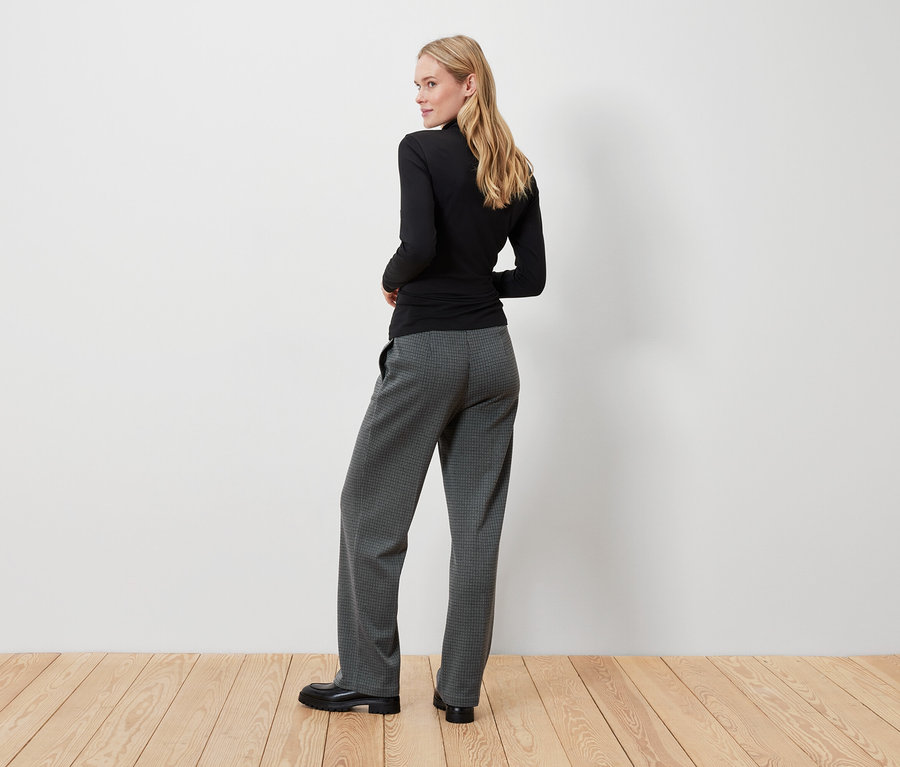 Blondýna v černém topu a šedých kalhotách se dívá přes rameno.