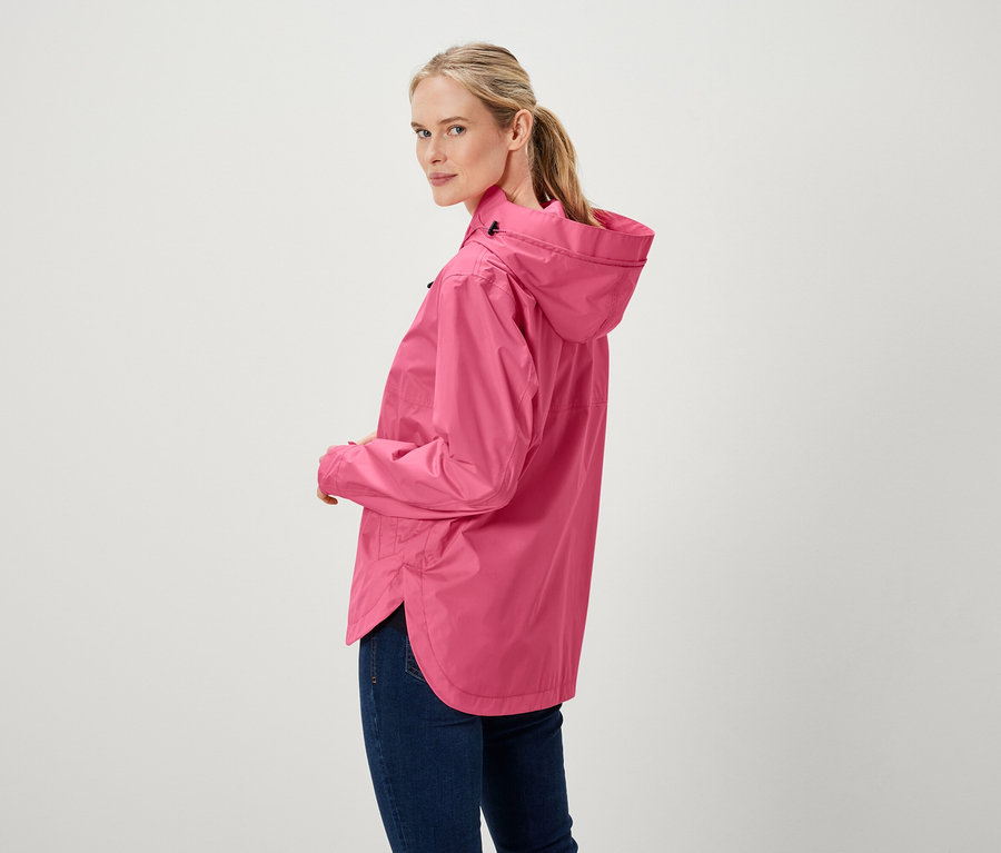 Žena se dívá přes rameno a má na sobě růžovou bundu a džíny.