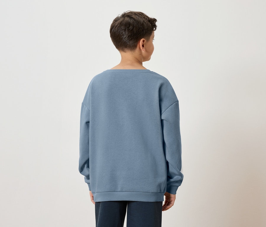 Pohled zezadu na chlapce s hnědými vlasy v modré mikině a tmavých kalhotách na bílém pozadí.