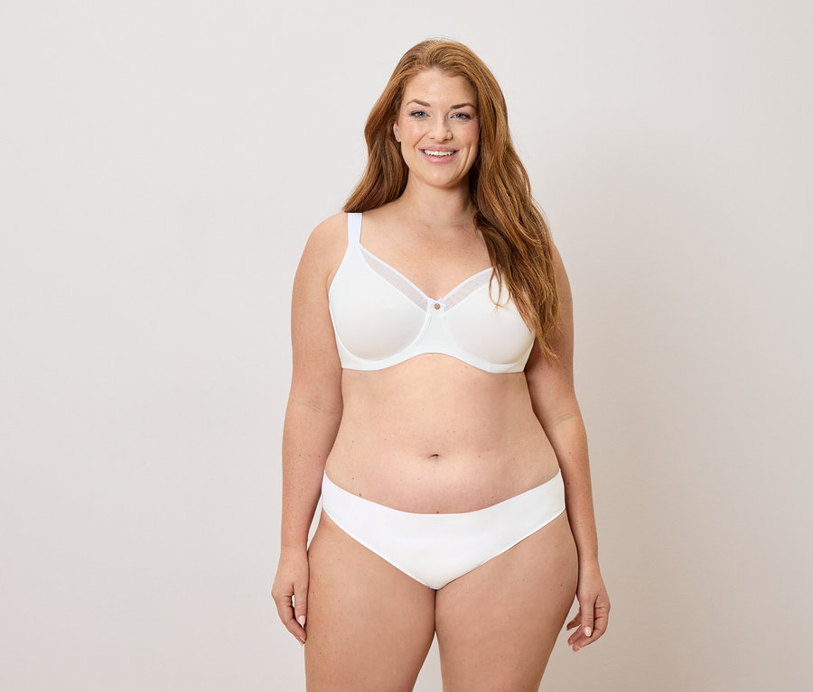 Usmívající se žena s dlouhými zrzavými vlasy v bílé podprsence a kalhotkách.