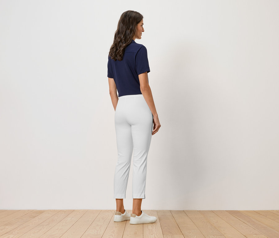 Žena stojí zády ke kameře, má na sobě tmavě modré polo tričko, bílé kalhoty a bílé boty.