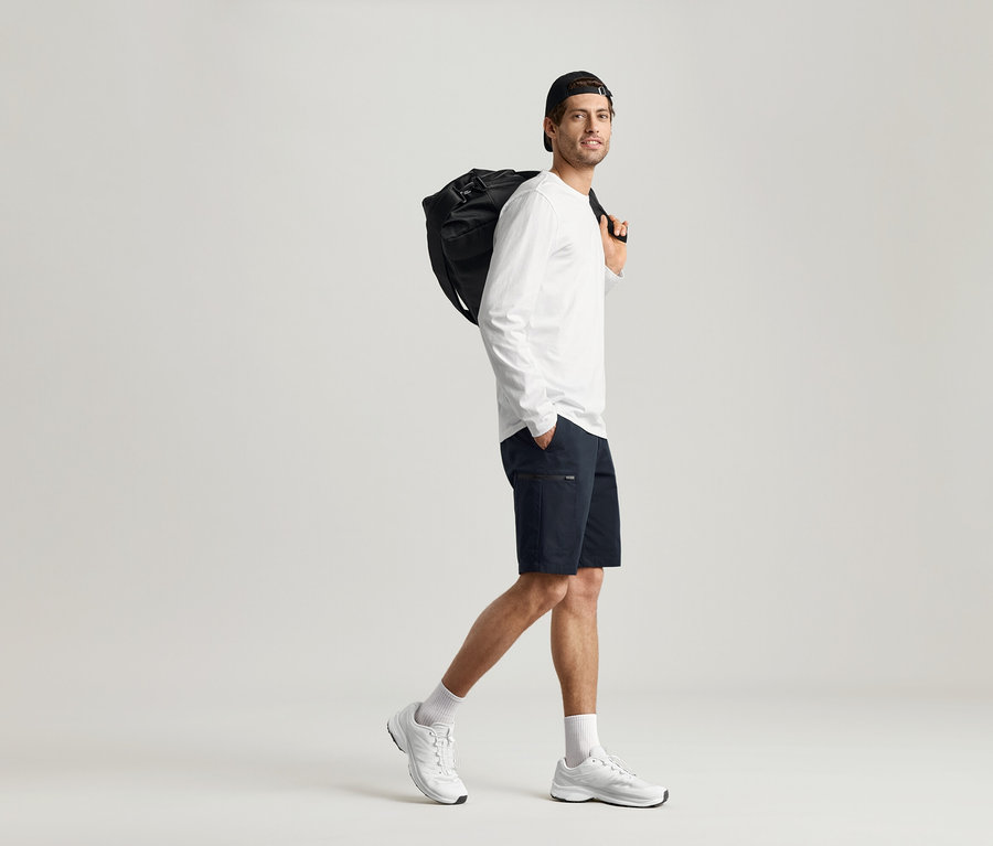 Muž jde s černou taškou přes rameno a má na sobě 2 Trika s dlouhým rukávem.