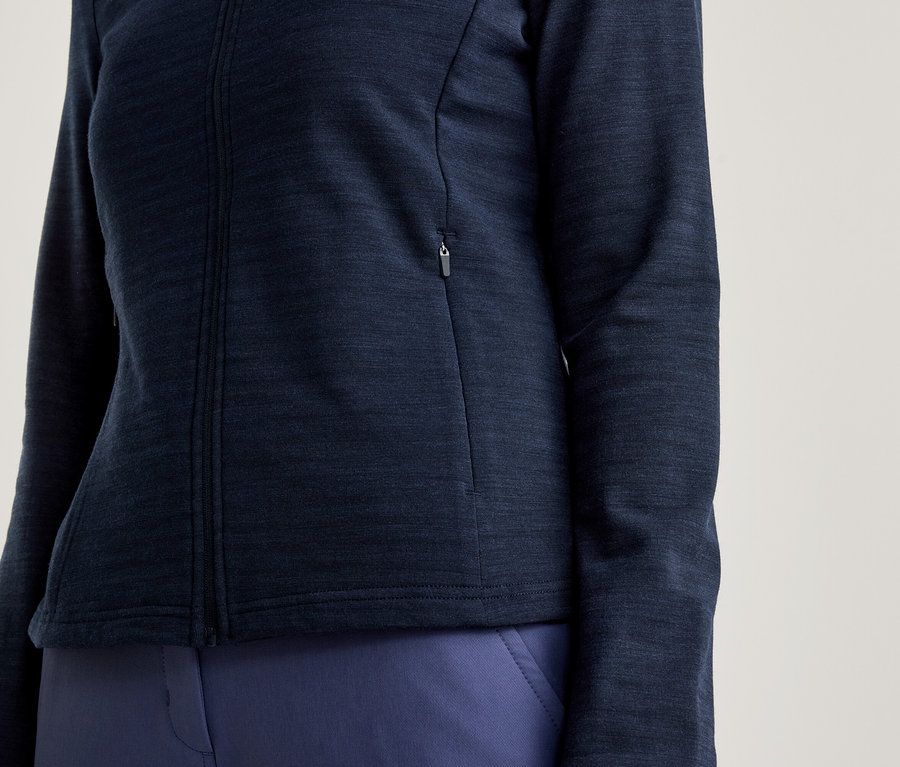 Detailní záběr ženy v tmavě modré bundě na zip a tmavě modrých kalhotách.