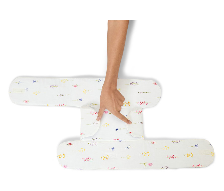 Ruka se dotýká bílého polohovacího polštáře s květinovým vzorem.