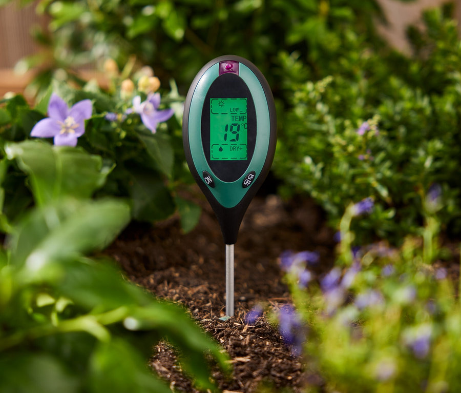 Zelený měřič půdy zapíchnutý v zemi mezi rostlinami.