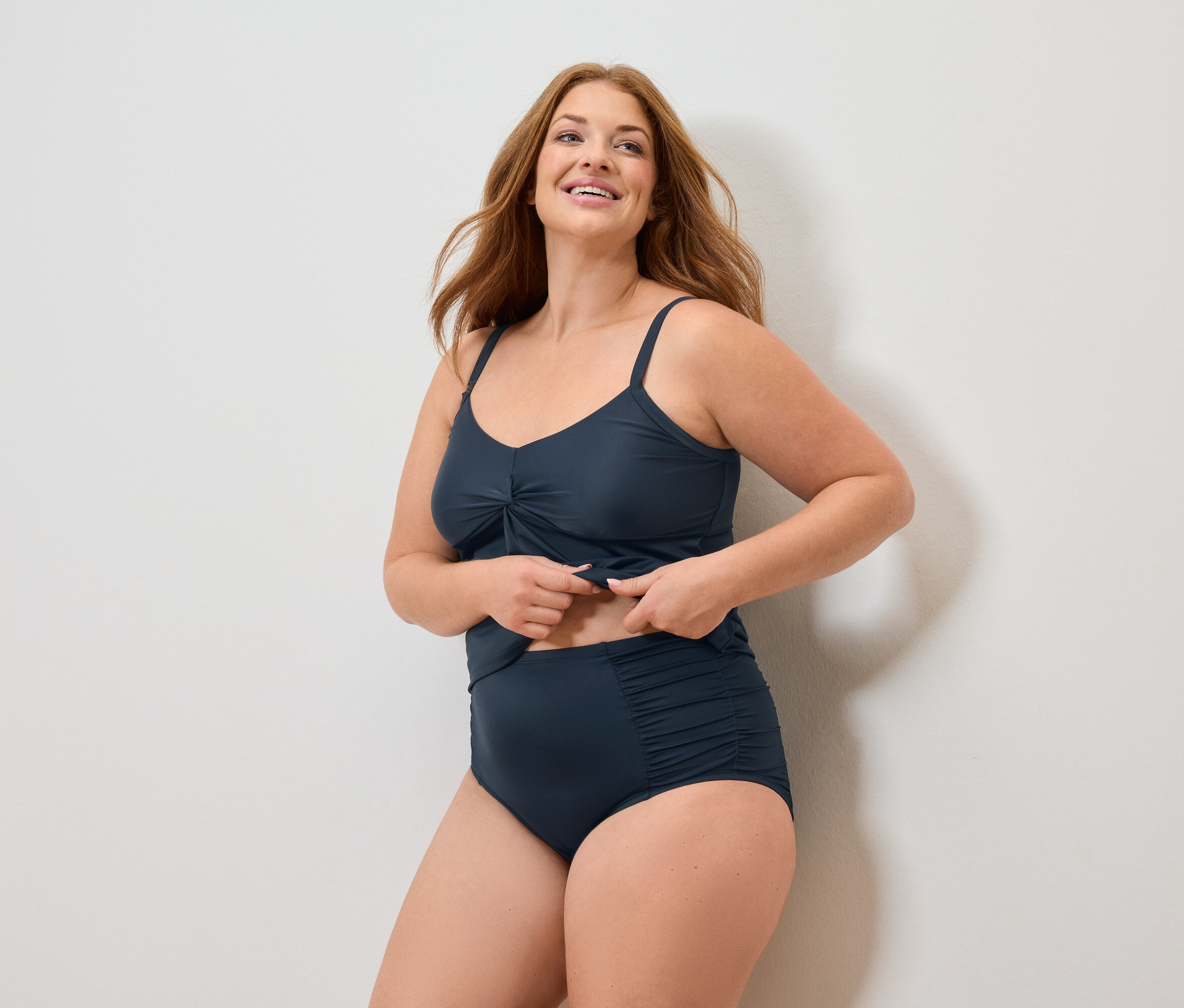 Žena s dlouhými rusými vlasy v tmavě modrých plavkách se usmívá.