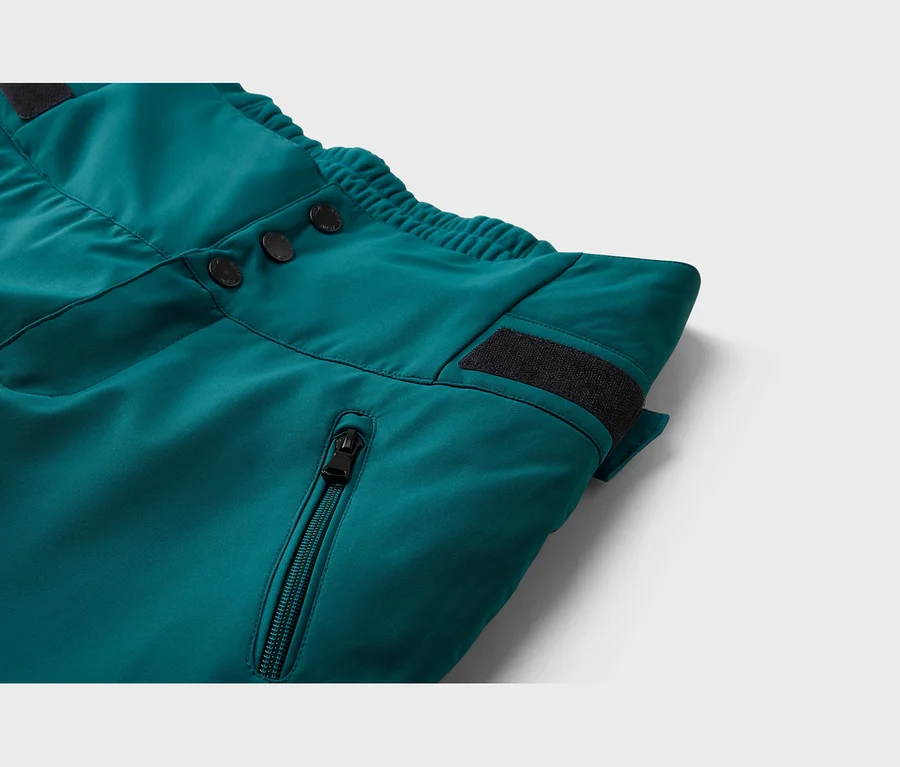 Detail tyrkysových kalhot, ukazující tři černé knoflíky, elastický pas, černý suchý zip a kapsu na zip.