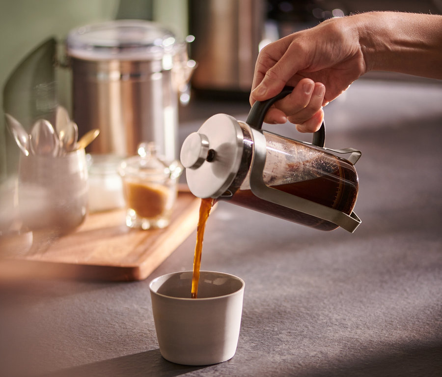 Ruka nalévá kávu z konvičky french press 300 ml stříbrné barvy do šálku.