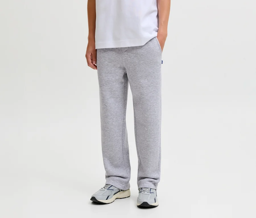 Osoba v šedých teplácích Jack & Jones Bradley, bílém tričku a šedých teniskách, s jednou rukou v kapse.