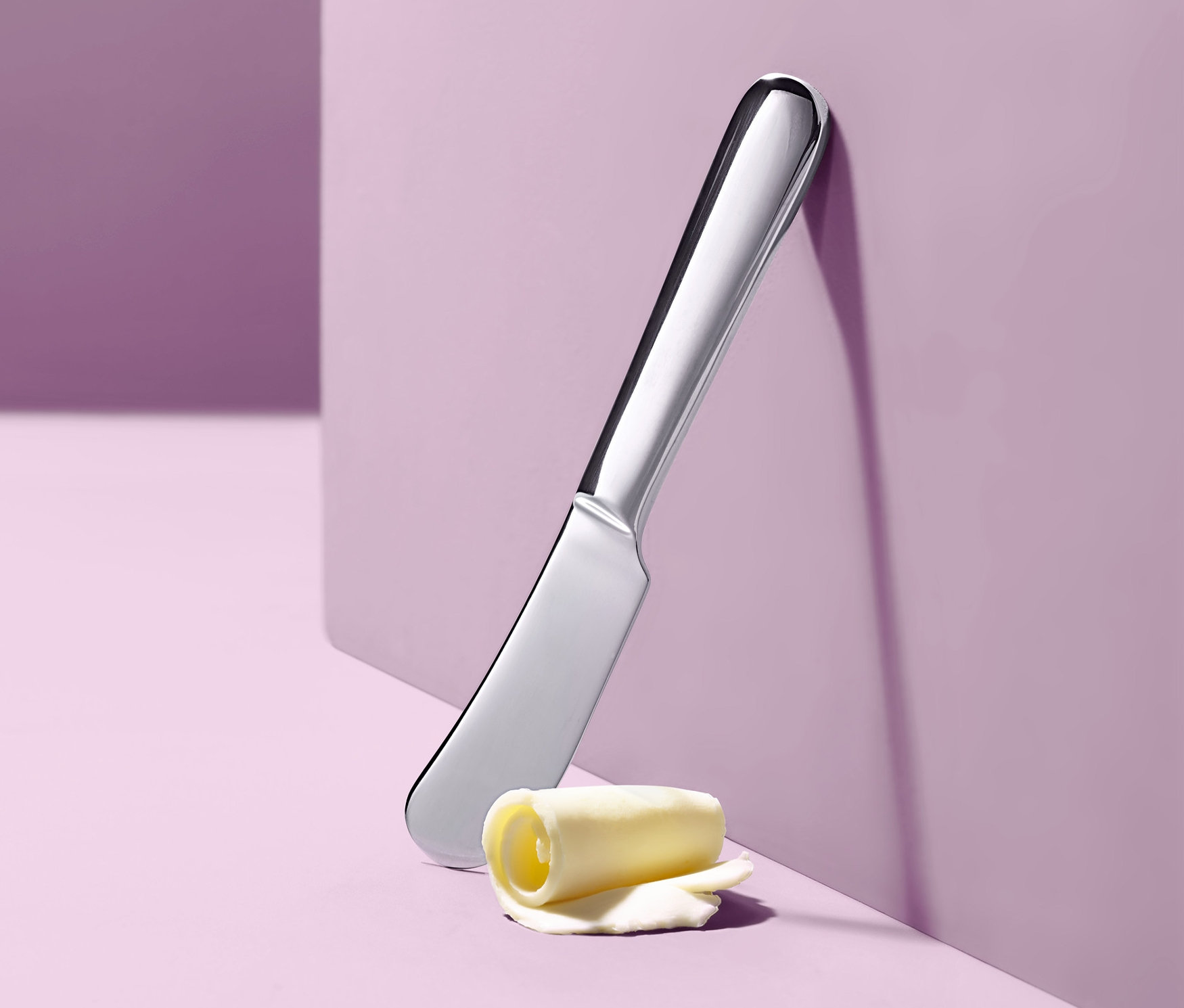 Nůž na máslo opřený o fialovou stěnu vedle rolky másla.