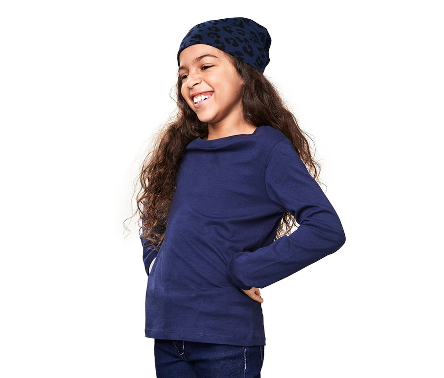 Usmívající se dívka s dlouhými vlnitými vlasy má na sobě modrou oboustrannou čepici s potiskem a modré tričko s dlouhým rukávem.