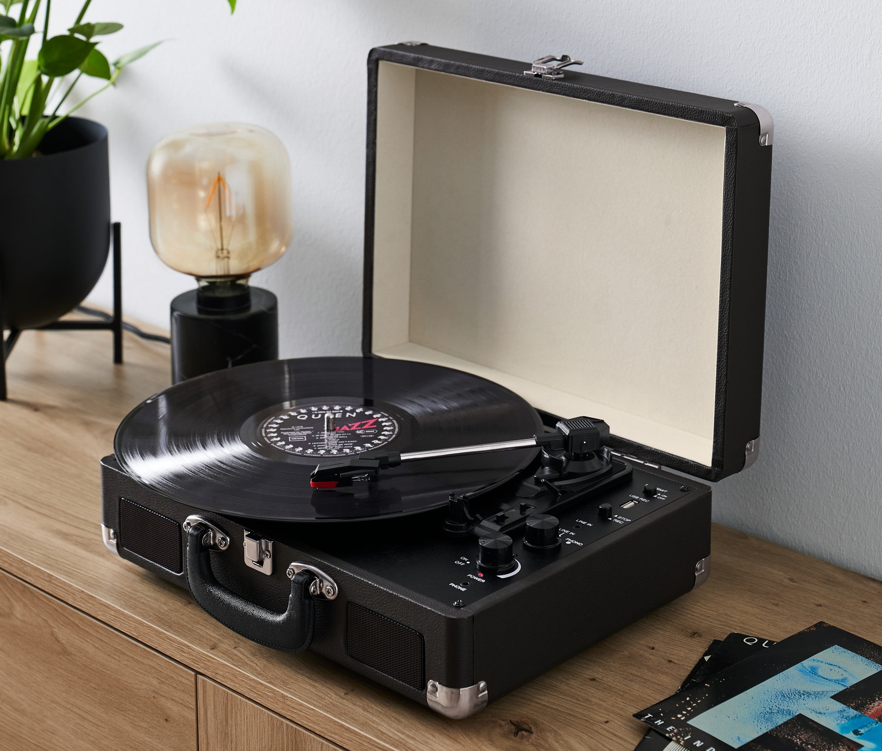 Černý retro gramofon s Bluetooth funkcí přehrává desku na dřevěné komodě.