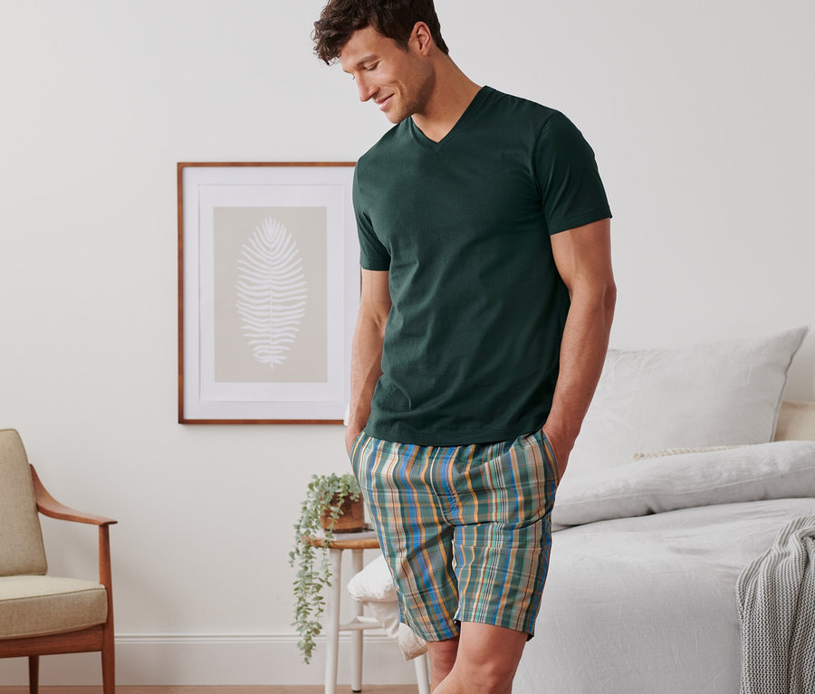 Muž v krátkém pyžamu stojí v ložnici.