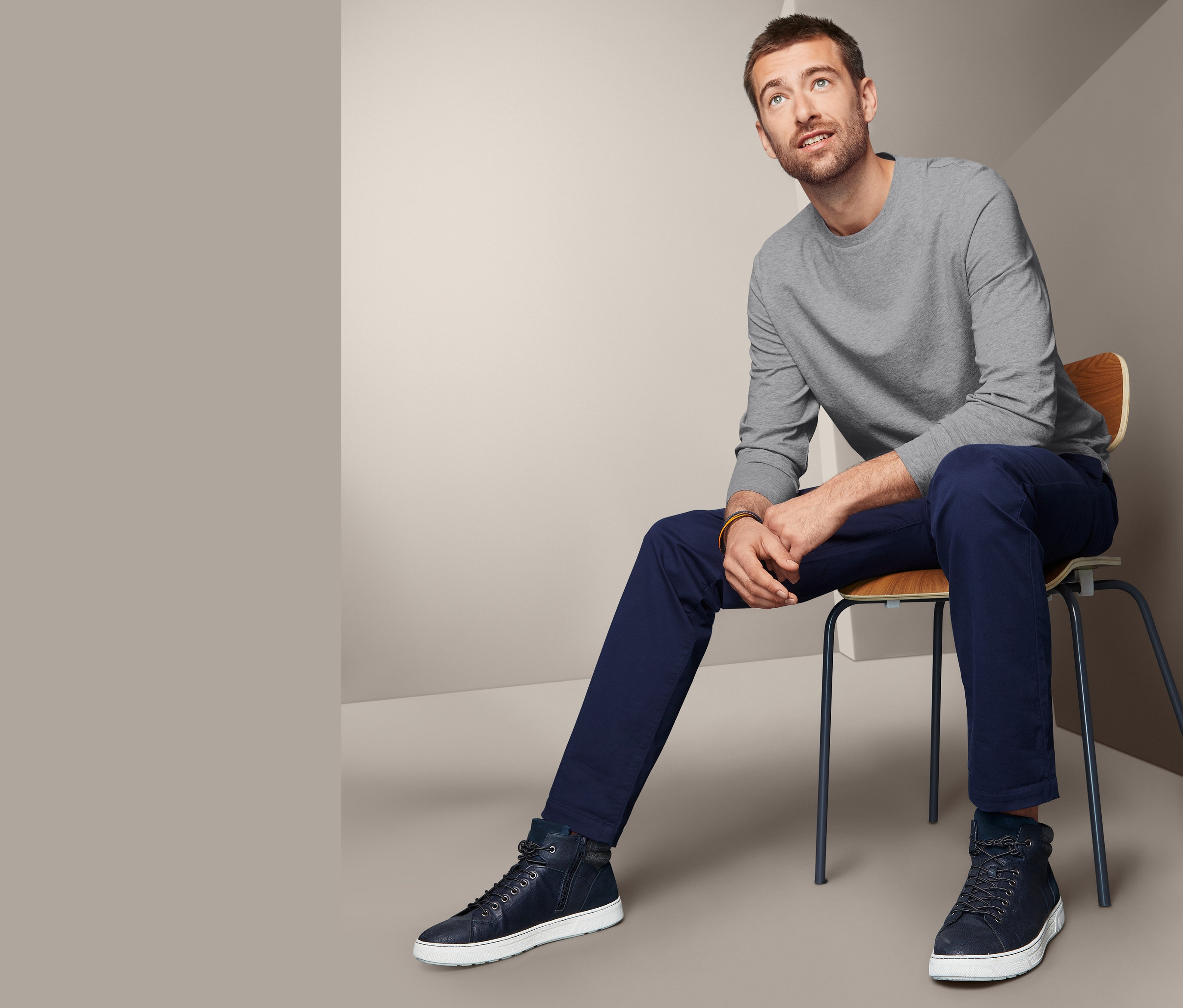 Muž sedí na židli a má na sobě šedé triko s dlouhým rukávem.