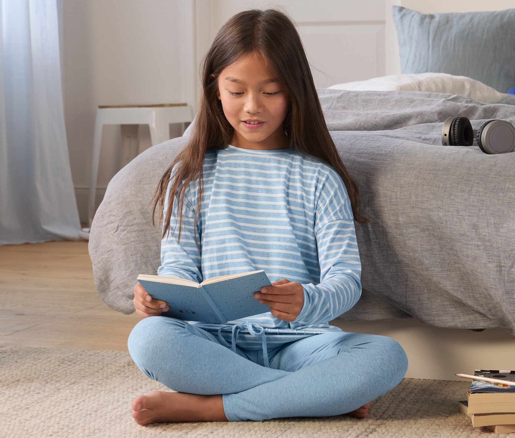 Dívka sedí na zemi a čte si knihu. Má na sobě světle modré dívčí pyžamo.