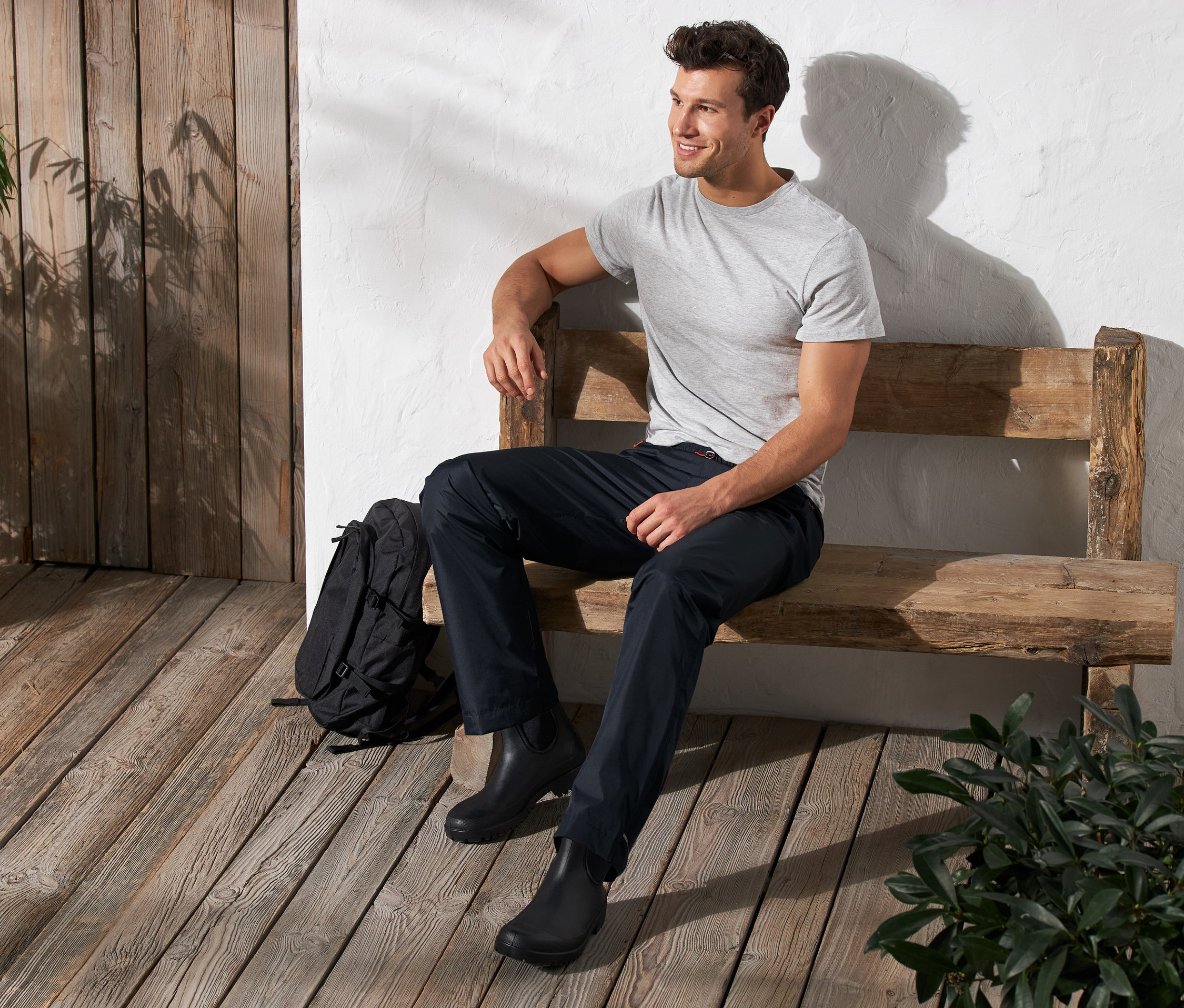 Muž sedí na lavičce a má na sobě unisexové kalhoty do deště.