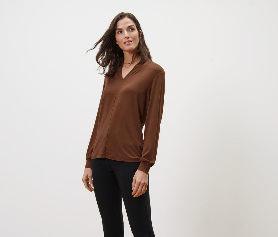 Žena má na sobě koňakové triko s dlouhým rukávem a výstřihem do V a černé kalhoty.