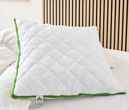 Na posteli leží bílý prošívaný polštář irisette® greenline s klimatickým pásem a zeleným lemováním.
