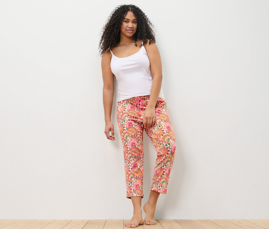 Žena opřená o stěnu má na sobě pyžamové kalhoty a tílko.