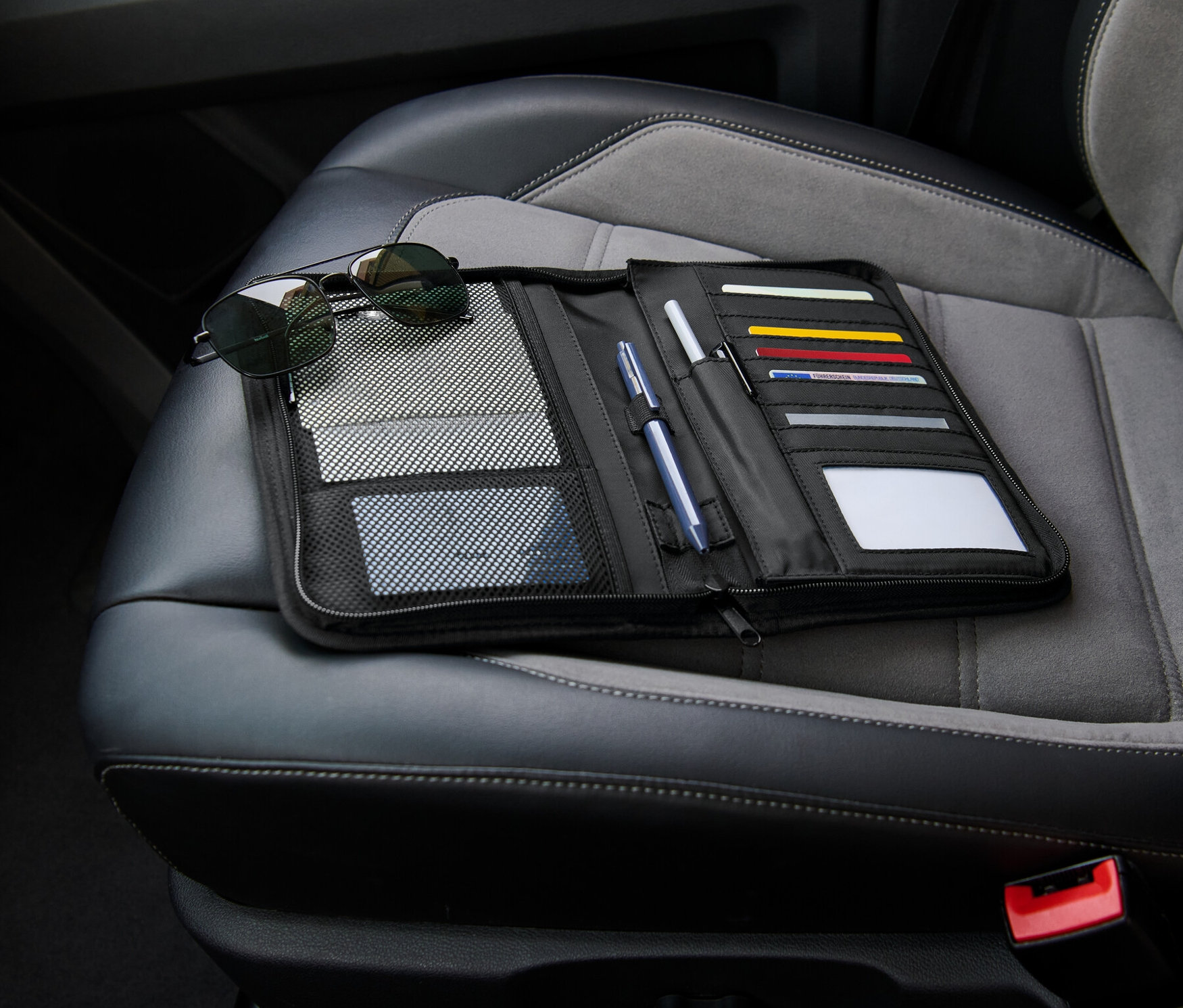 Černý organizér do přihrádky v palubní desce leží otevřený na sedadle auta vedle slunečních brýlí.