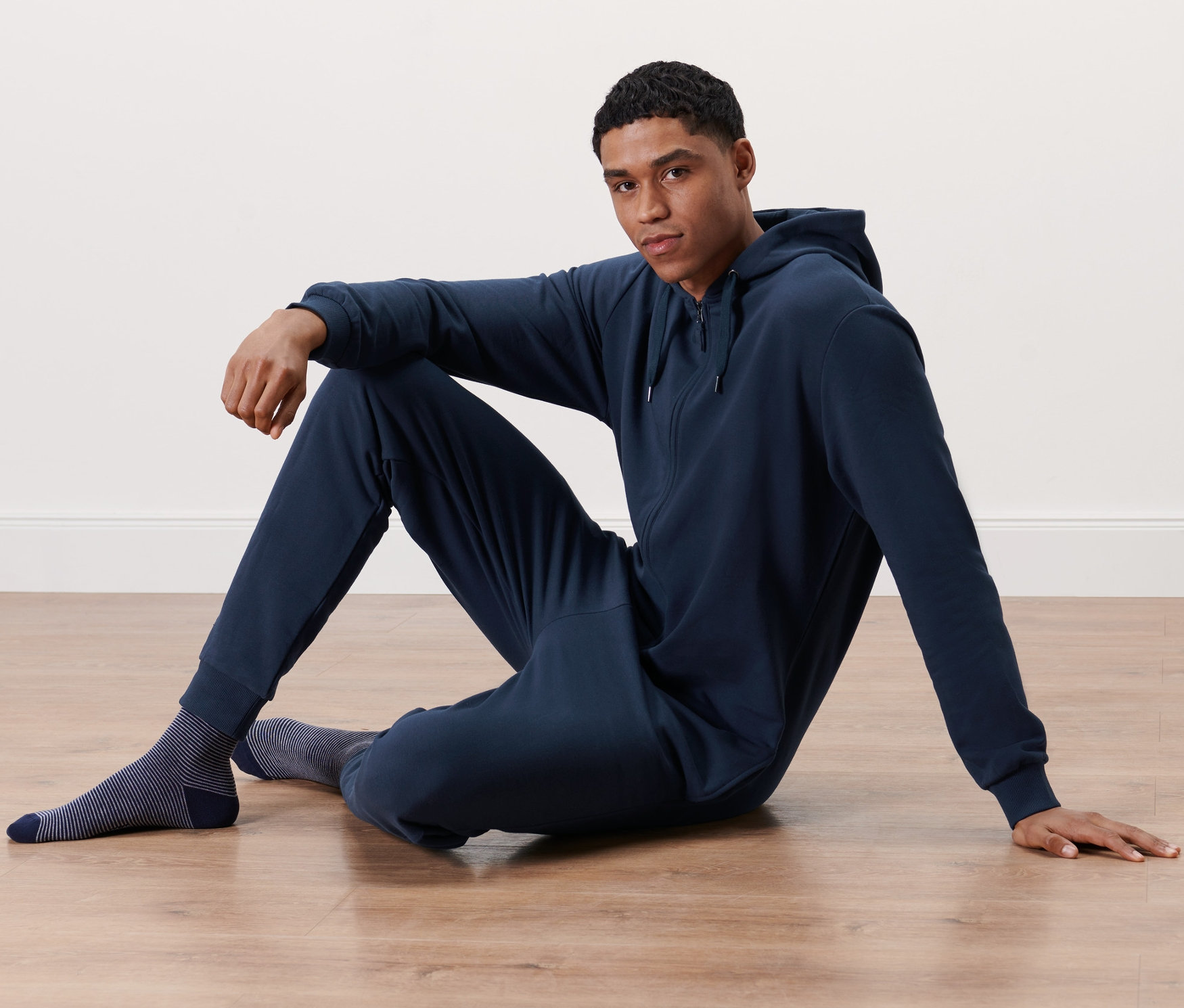 Muž sedí na podlaze v tmavě modrém domácím overalu.