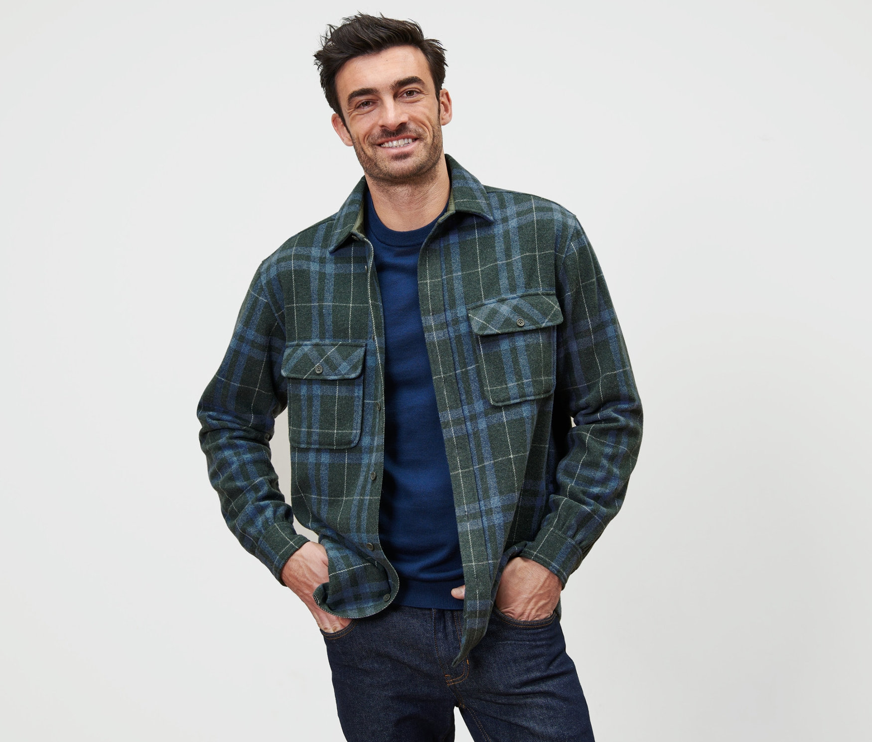 Muž pózuje v zelené a modré kostkované flanelové košilové bundě.