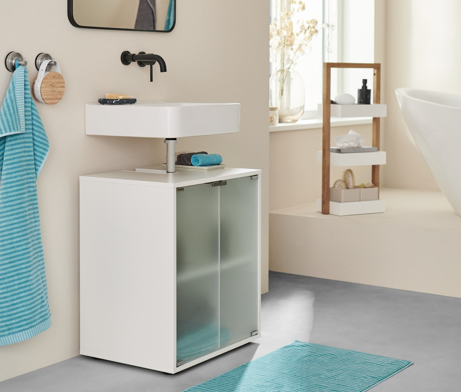 Koupelna s umyvadlovou skříňkou, modrozelenou předložkou a ručníky.