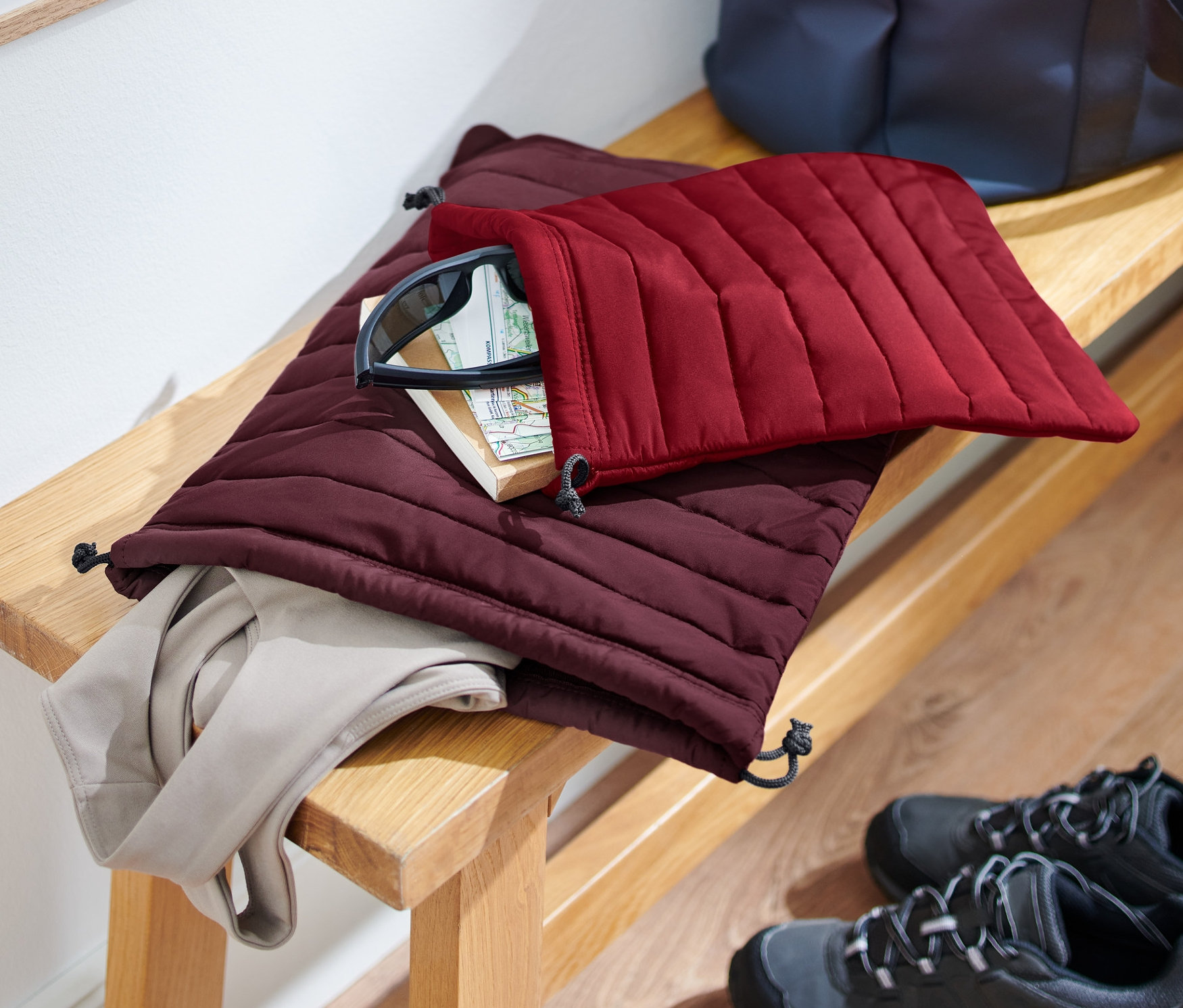 Na lavici leží 2 prošívané organizéry, jeden bordó a jeden vínové barvy, s obsahem. Boty stojí na podlaze.