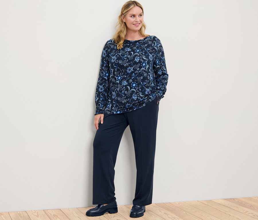 Žena pózuje na sobě halenkové triko s potiskem a pohodlné žerzejové kalhoty.