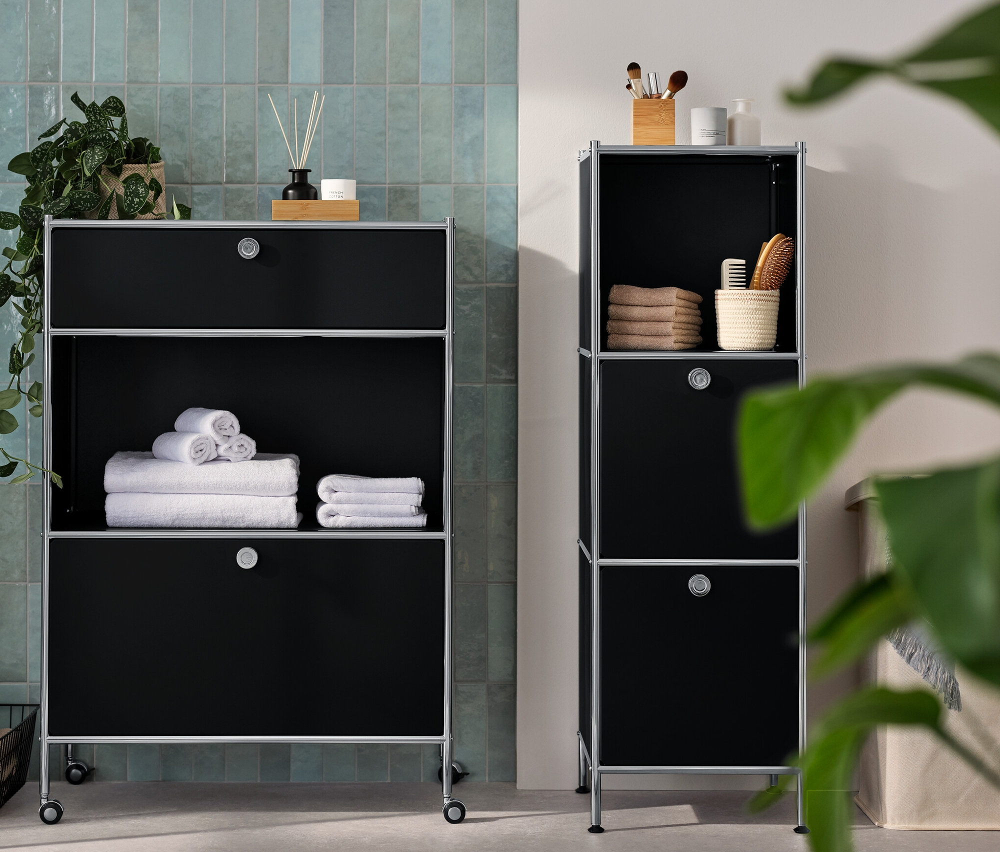 Černá kovová komoda »CN3« s 1 zásuvkou a 1 výklopnými dvířky a úzká komoda »CN3« se 2 výklopnými dvířky. V koupelně jsou ručníky a doplňky.