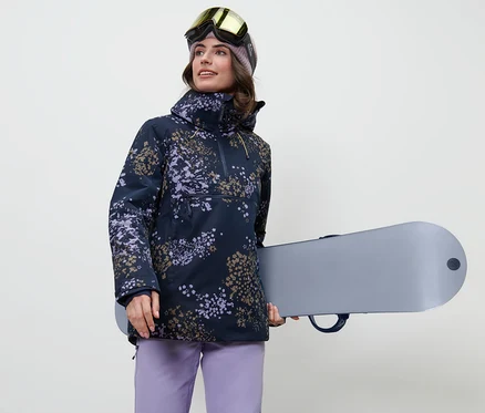 Žena drží snowboard a má na sobě lyžařskou bundu s krátkým zipem.
