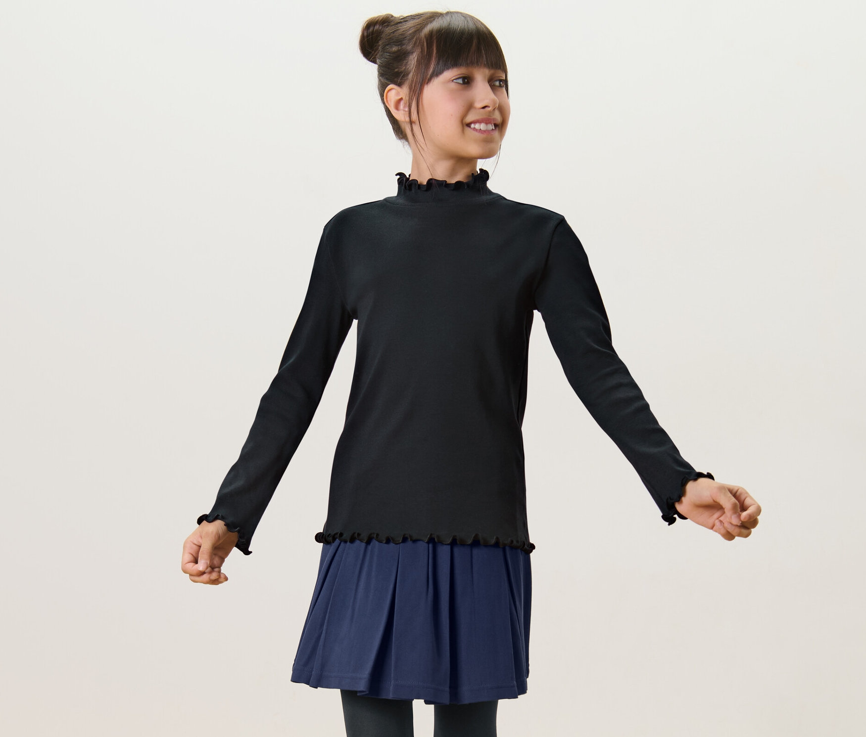 Dívka má na sobě černé triko s dlouhým rukávem a modrou sukni.