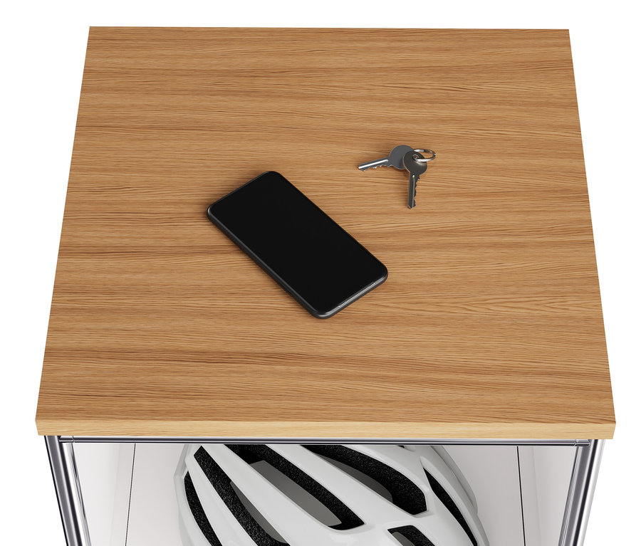 Na dřevěné desce úzké bílé kovové komody »CN3« leží mobilní telefon a klíče. Ve výklopném prostoru je helma.