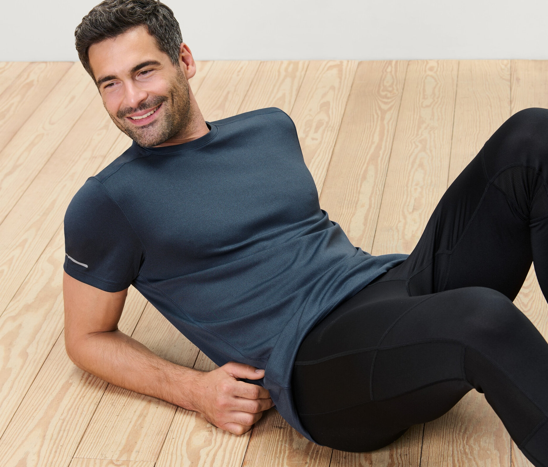 Muž leží na dřevěné podlaze a má na sobě modré melírované funkční tričko.