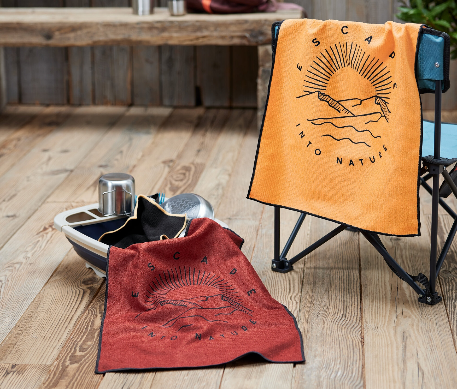 Oranžová utěrka na židli a červená utěrka v míse. V pozadí je batoh a termoska.