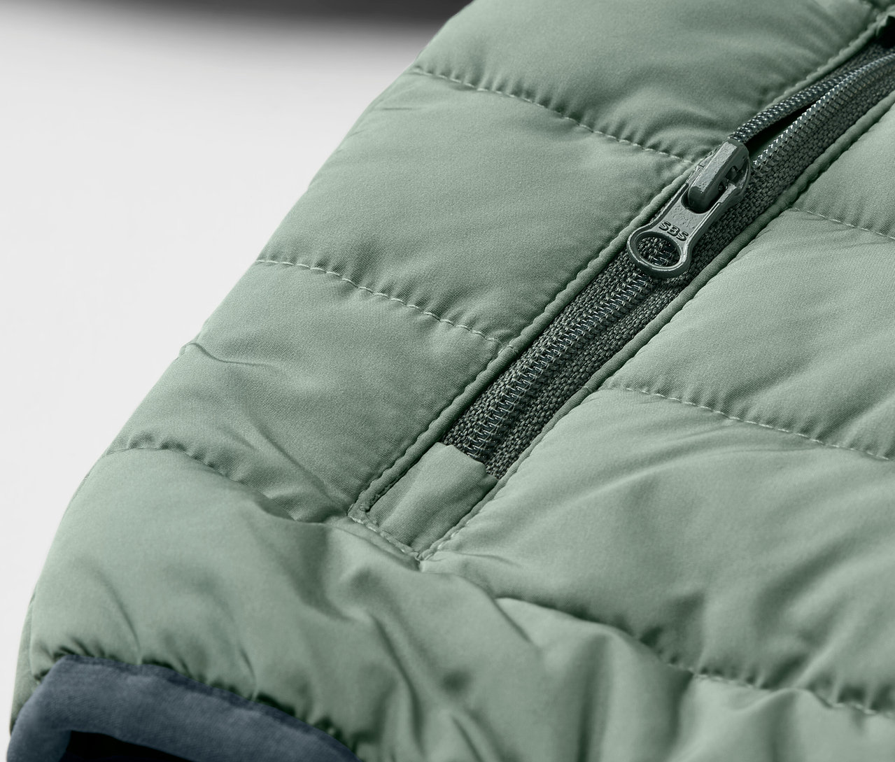 Detail zelené dětské prošívané bundy se zipem.