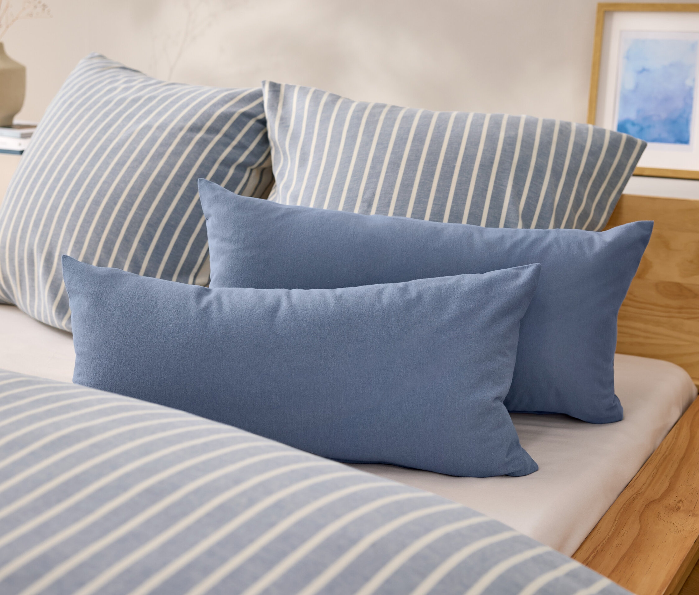 Na posteli jsou dva modré obdélníkové polštáře a dva polštáře s modrými a bílými pruhy.