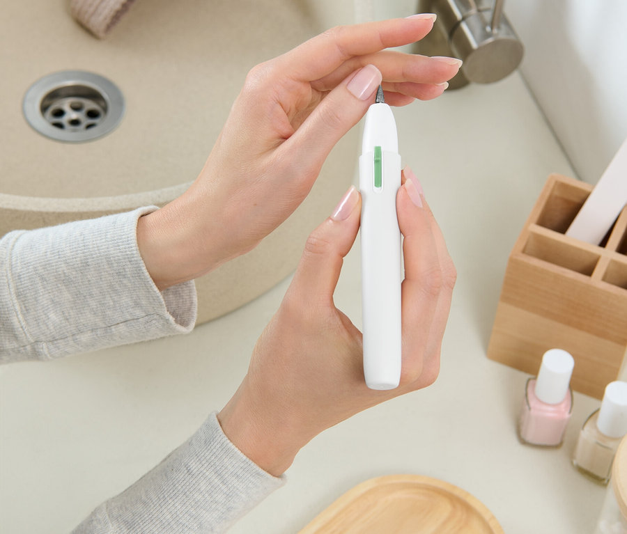 Žena drží bílou frézku na nehty před umyvadlem.