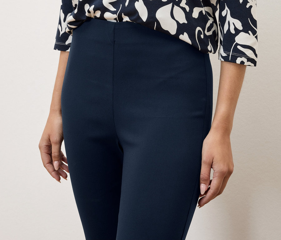 Detailní záběr ženy v tmavě modrých kalhotách a halence s květinovým vzorem.