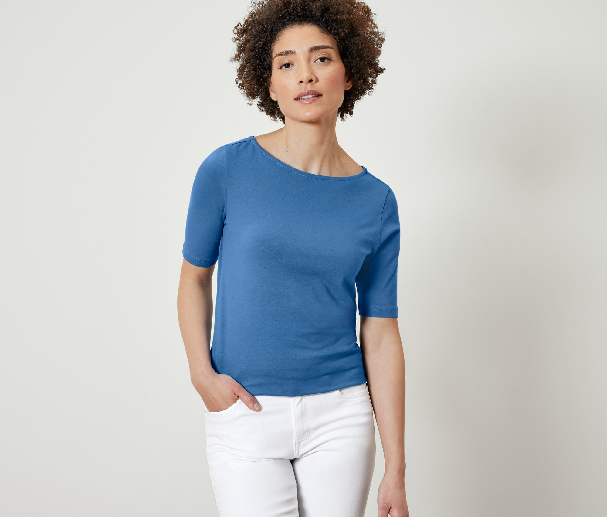 Žena pózuje v modrém tričku s polodlouhým rukávem.
