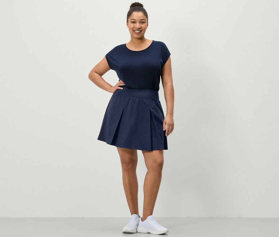 Žena pózuje ve sportovní sukni tmavě modré barvy a modrém sportovním tričku.