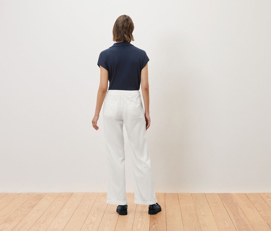 Žena stojí zády, má na sobě tmavě modré polo tričko a bílé kalhoty.