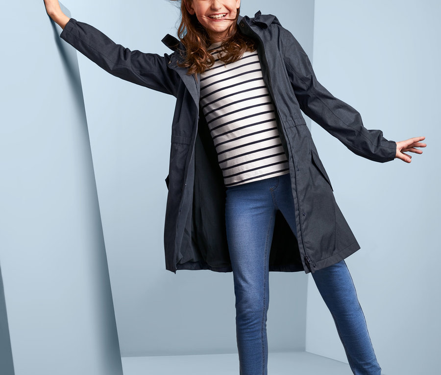 Dívka pózuje v bundě do každého počasí v džínovém vzhledu, pruhovaném tričku, džínách a holínkách.