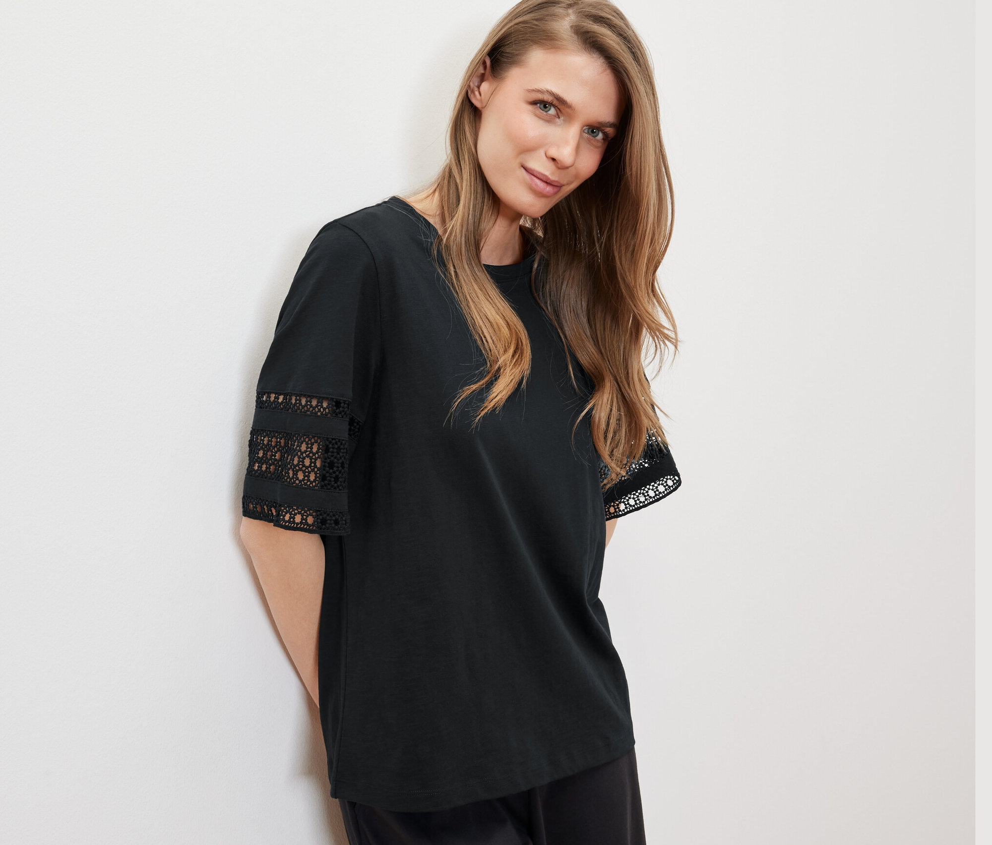 Žena opřená o zeď má na sobě černé triko s výšivkou.