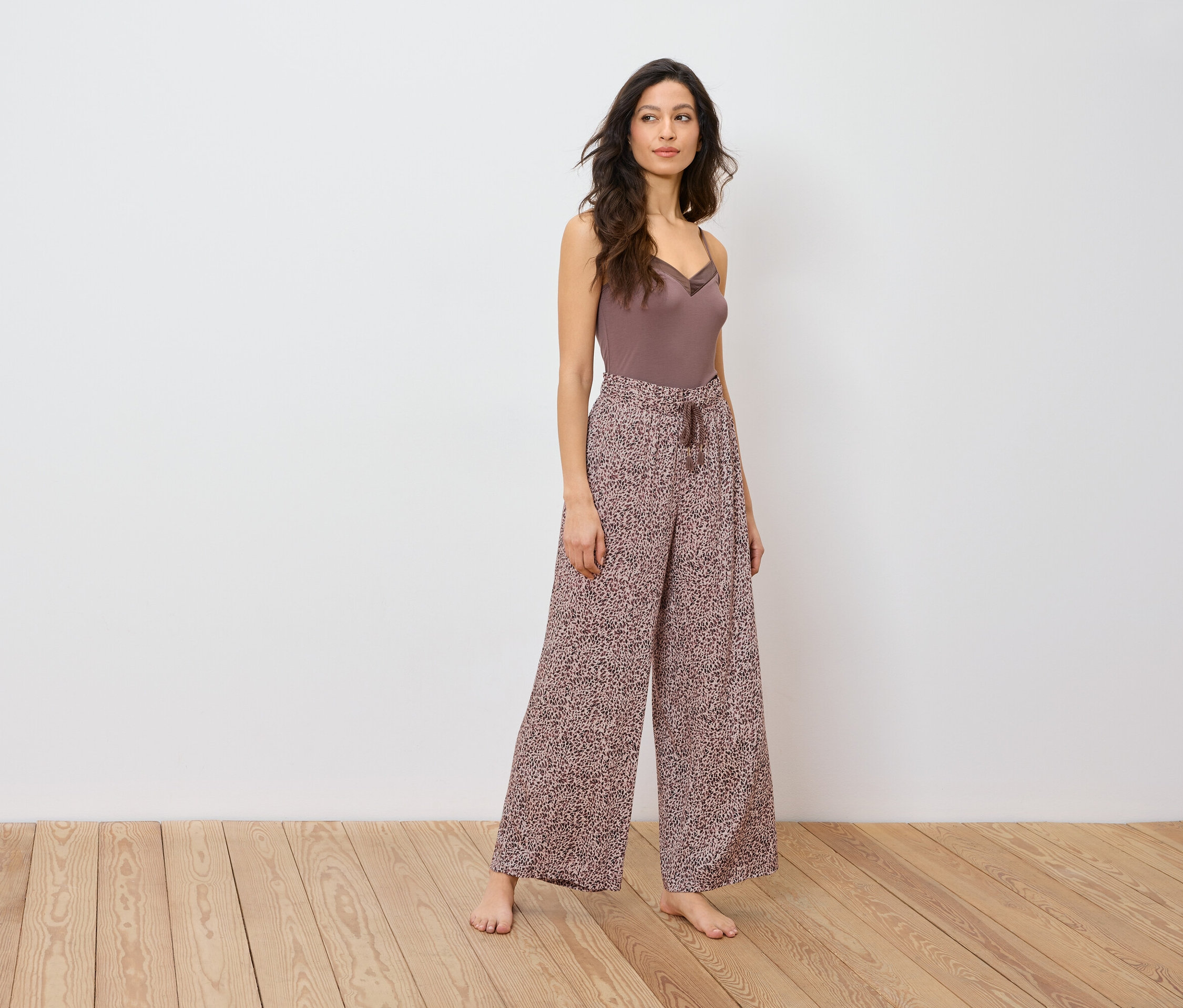 Žena pózuje v hnědém topu a širokých kalhotách se zvířecím potiskem.