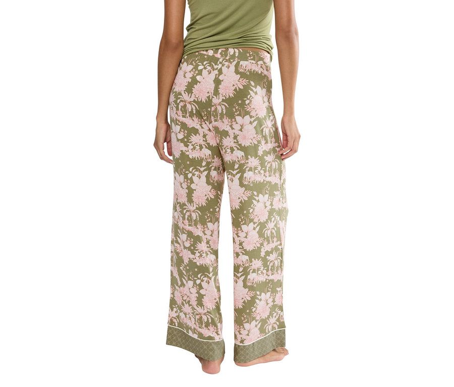 Pohled zezadu na ženu v zelených kalhotách s růžovým květinovým vzorem a zeleném topu.