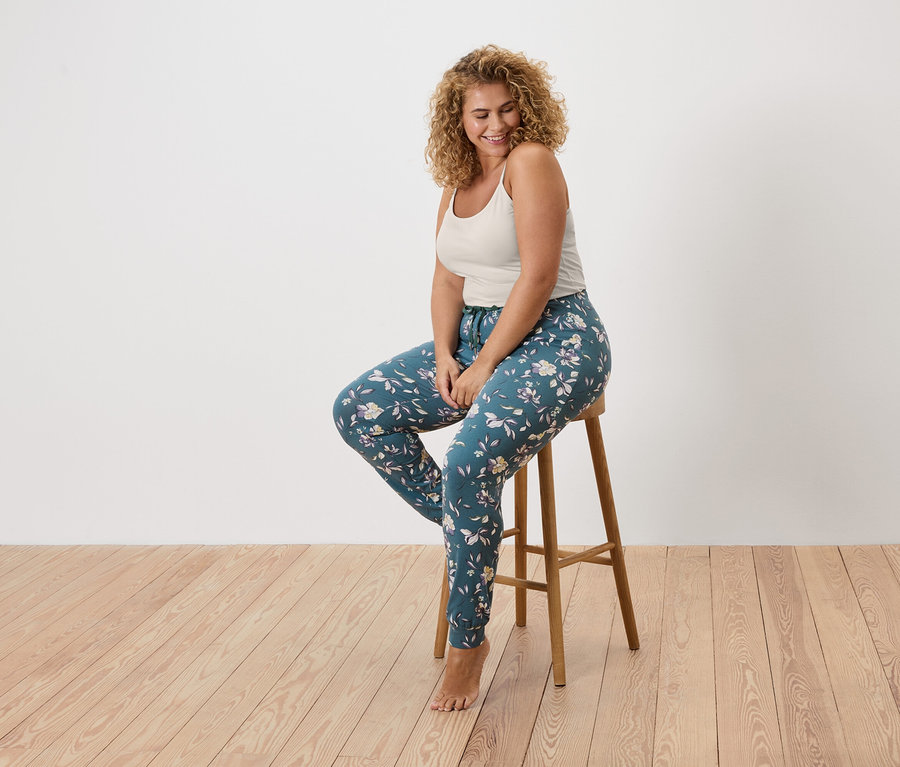 Žena s kudrnatými vlasy sedí na stoličce a má na sobě tílko a květinové legíny.