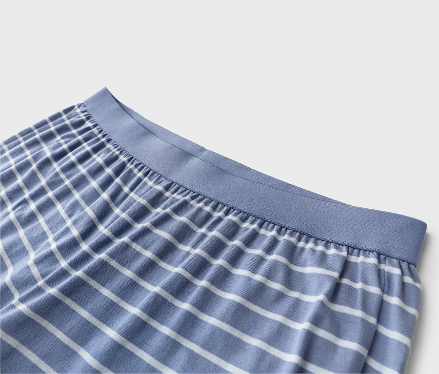 Detailní záběr na modro-bílé pruhované pyžamové kalhoty s modrým elastickým pasem.