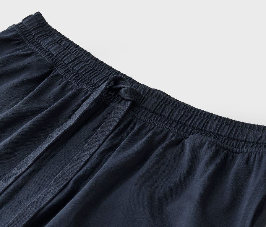 Detailní záběr na tmavě modré látkové kalhoty se stahovací šňůrkou.